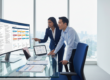 Modern office in Singapore with diverse pros collaborating at monitor, cityscape backdrop.